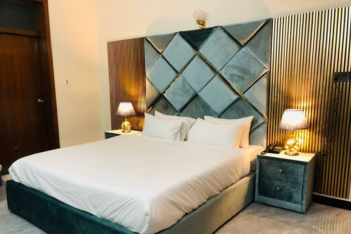 A neatly made bed with white linens, a dark teal upholstered headboard, and two bedside tables with lamps.