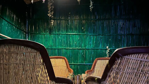 Wicker stoelen met een geweven zitvlak en rugleuning, geplaatst voor een groene muur met verticale lijnen.