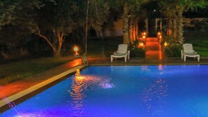 A swimming pool with a water feature, surrounded by palm trees and lounge chairs. - Jnane Riad (Ghmate)