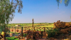 A well-maintained garden with a stone pathway, rustic wooden structures, and a clear view of the surrounding landscape. - Jnane Riad (Ghmate)