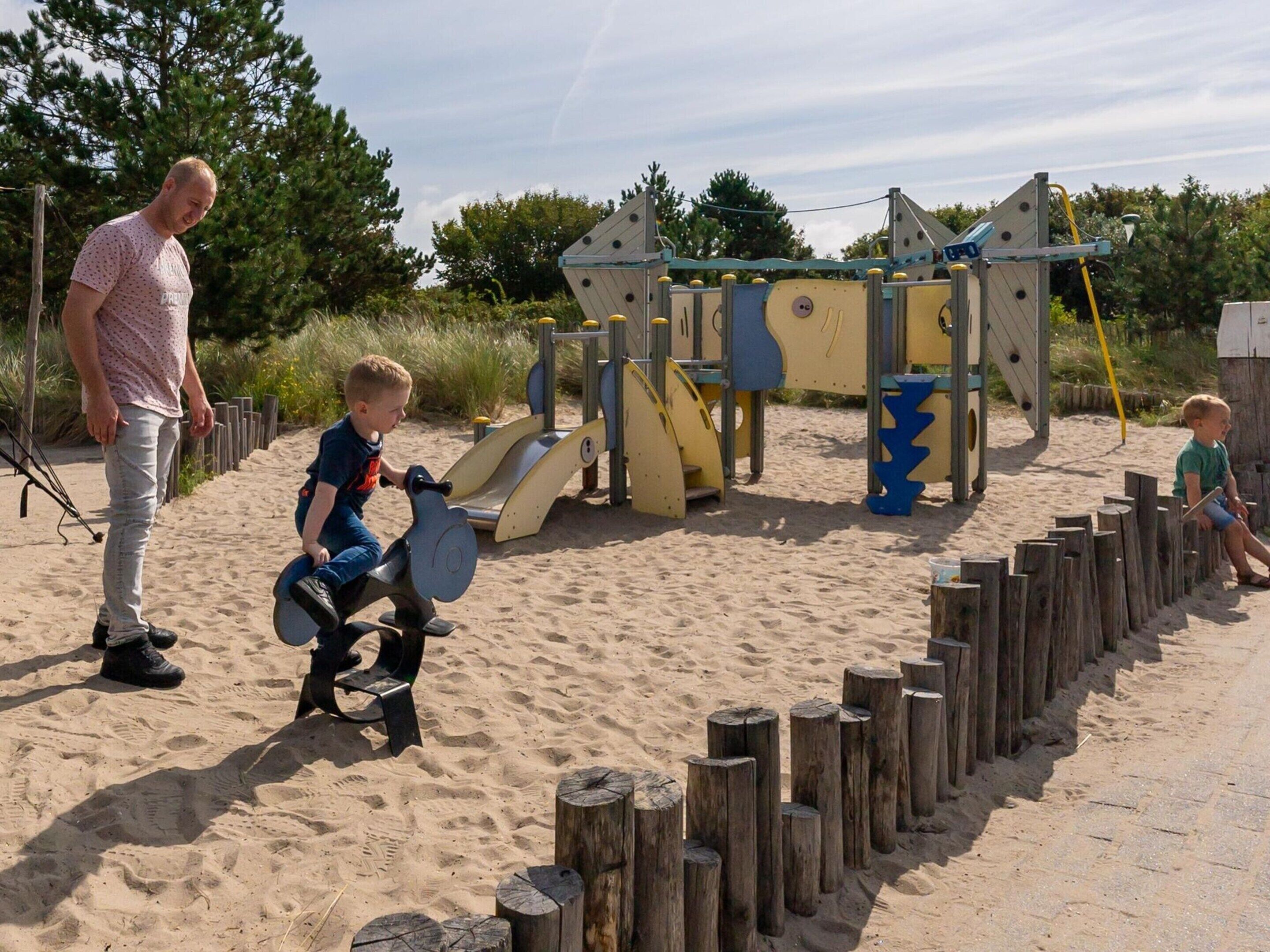 Een zanderig strand met een speeltuin, inclusief glijbanen en klimconstructies.