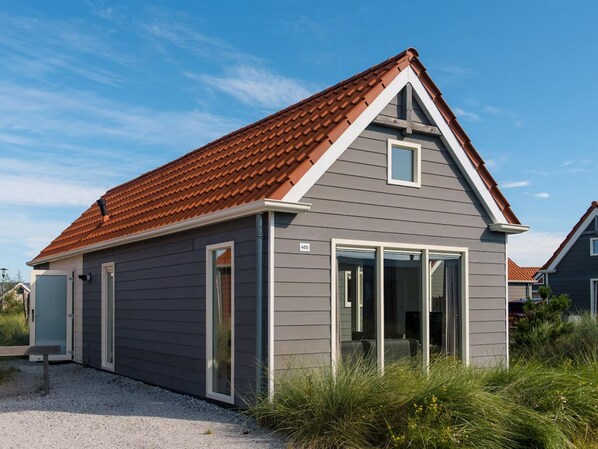 A modern house with a grey siding exterior, a red-tiled roof, and a small porch with a bench. - Cozy Lodge by Hollum (Hollum)