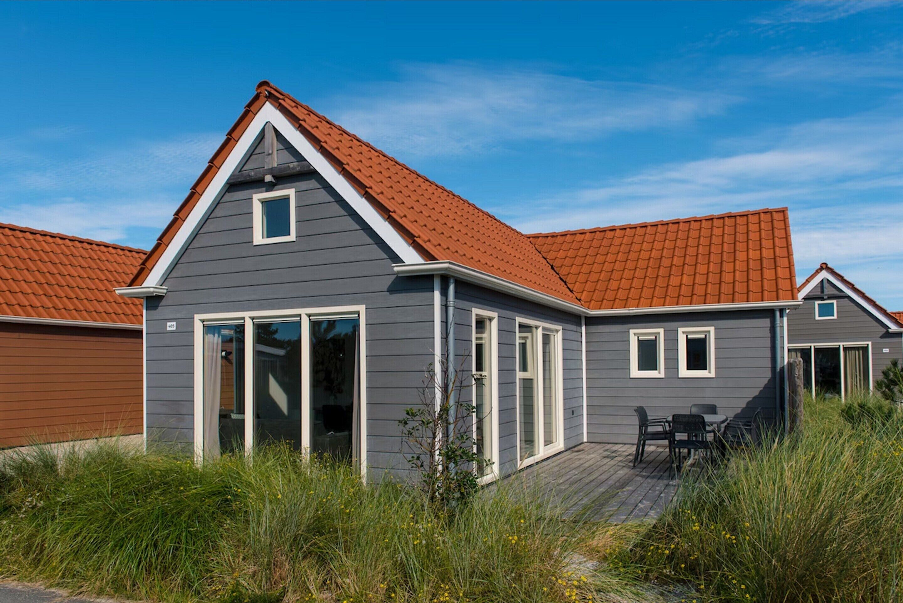 A modern house with a grey exterior, red roof, and large sliding glass doors.
