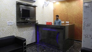 A reception area with a counter, a television, and a fan on the wall. - Hotel Kanak Palace By GRB (New Delhi)
