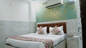 A bedroom with a bed, a nightstand, an air conditioning unit, and a patterned wall. - Hotel Kanak Palace By GRB (New Delhi)