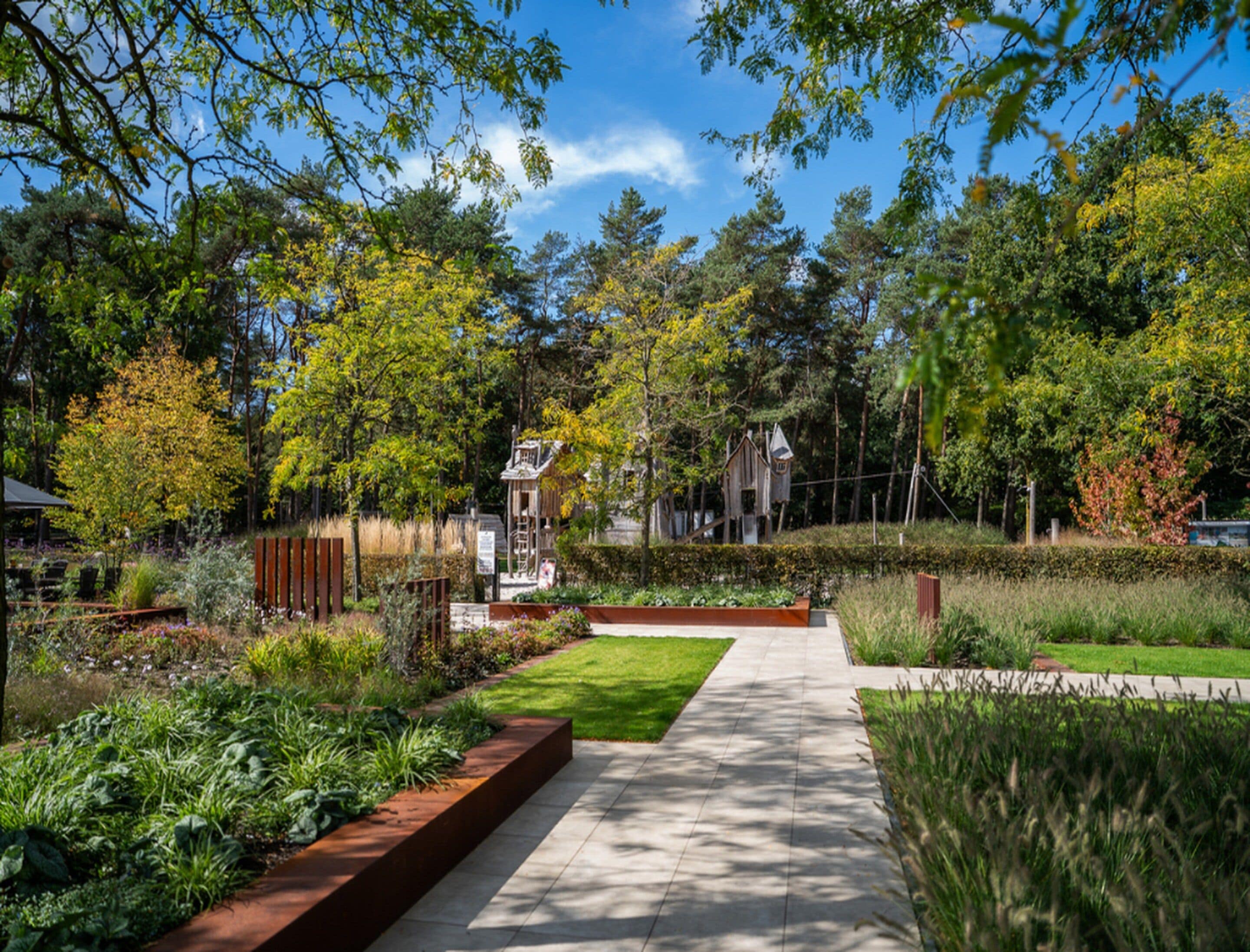Un sendero en un jardín con cerca de madera, una pequeña construcción de madera y diversas plantas.