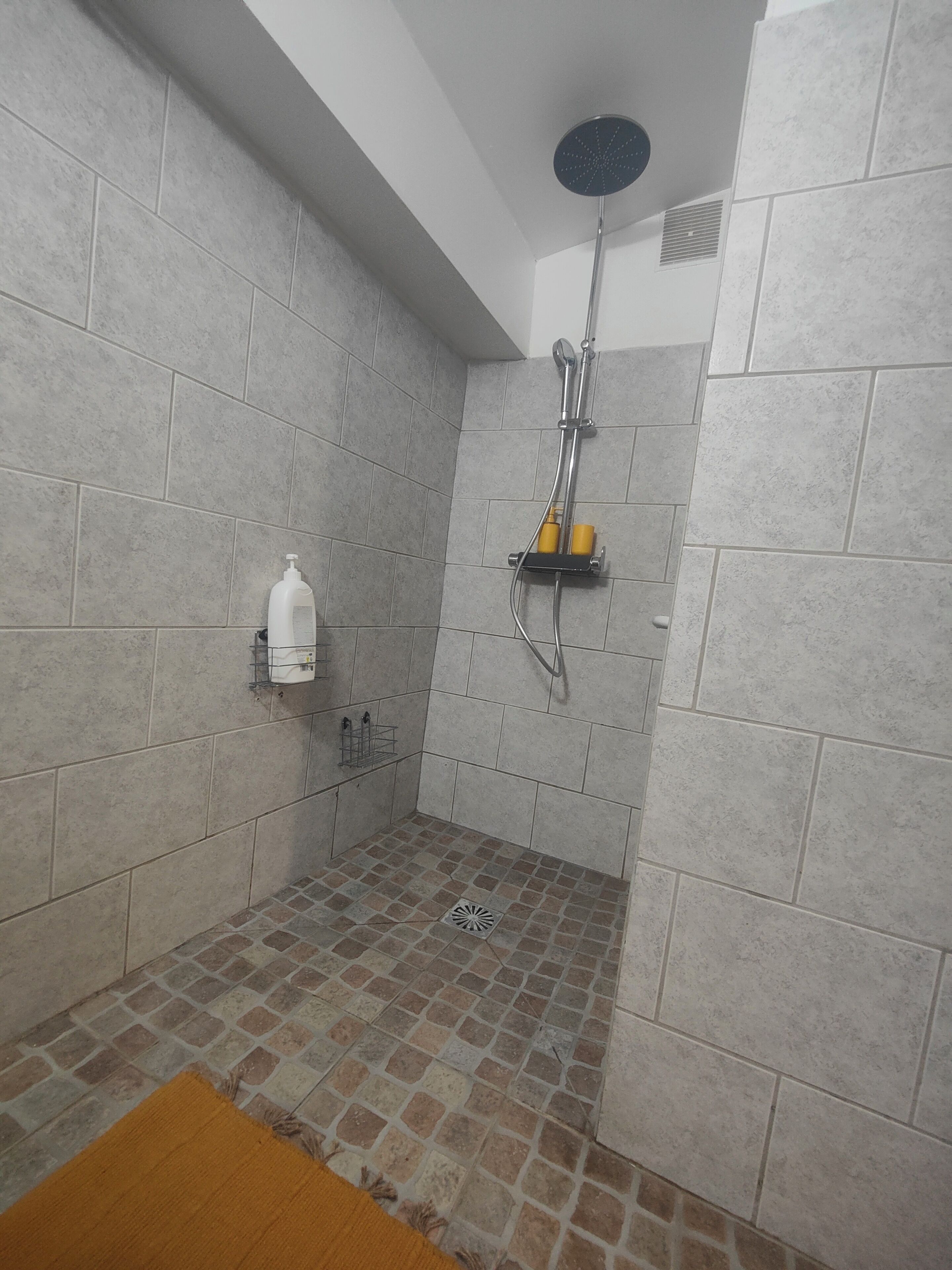 A shower with a handheld showerhead, a wall-mounted shelf with toiletries, and a towel rack.
