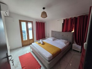 A bedroom with a bed, a red rug, a wooden door, and a window.