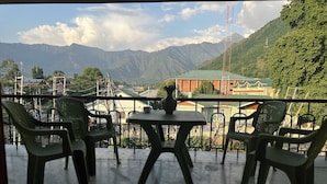 A balcony with chairs and a table, overlooking a mountainous landscape with buildings in the background. - Jan Mahal (Srinagar)