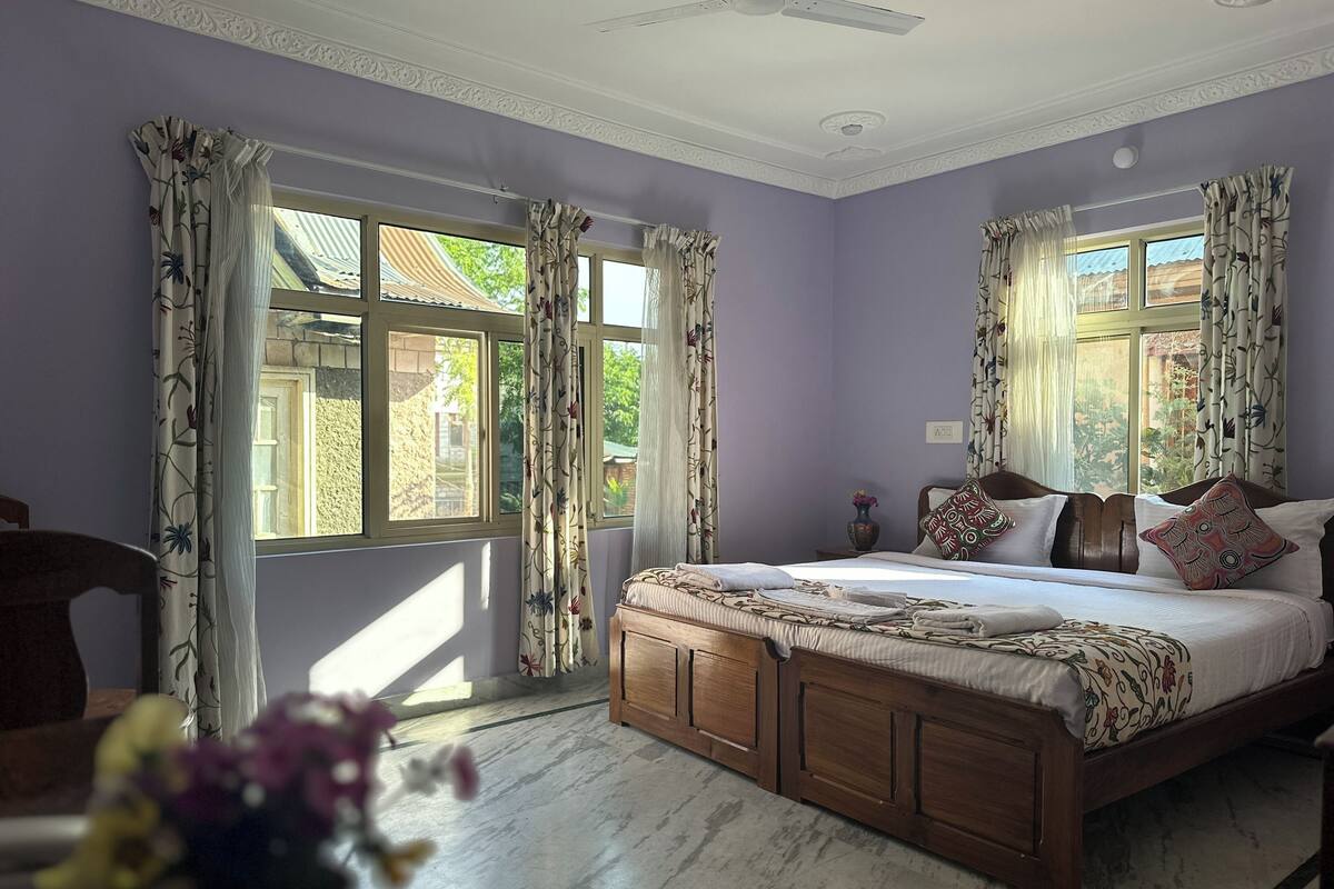 A bedroom with a wooden bed, floral curtains, and a view of greenery outside.