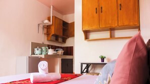 A hotel room with a neatly made bed, a red and floral bedspread, a wooden cabinet above the bed, and a small table with a plant.