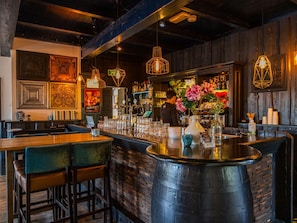 Un espace bar doté d’un comptoir en bois, de plusieurs options d’assises et d’un éclairage décoratif.