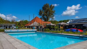 Ein Schwimmbecken mit Liegestühlen und Sonnenschirmen, umgeben von Gebäuden und Bäumen.