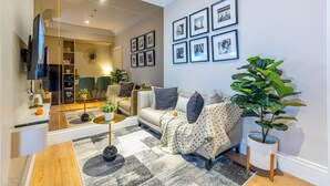 A modern living room with a sofa, a coffee table, a TV, and a large mirror. There are framed pictures on the wall and a potted plant. - Roseville SOHO and Suites by Nagisa Bali (South Tangerang)