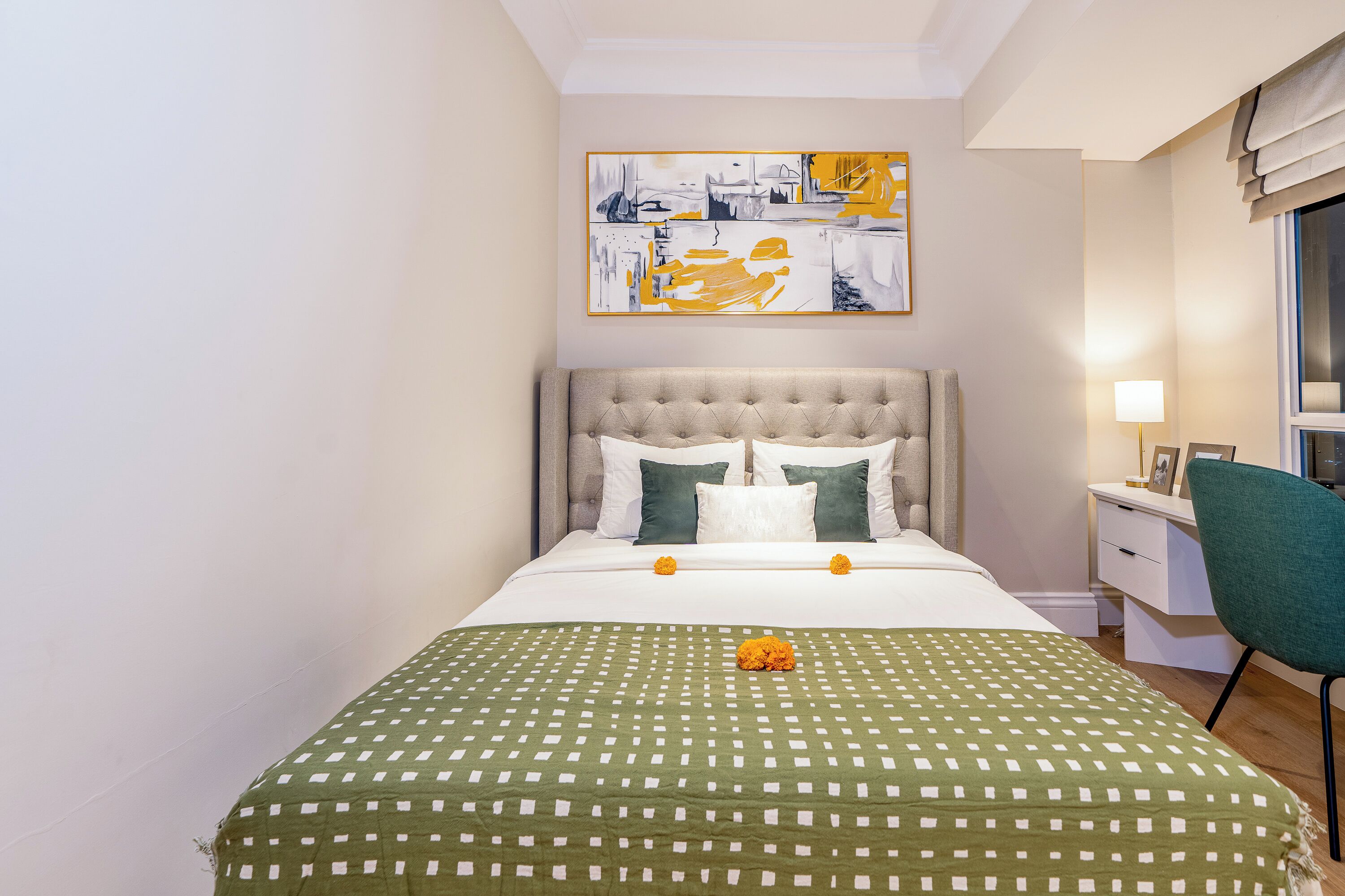 A neatly made bed with a green checkered bedspread, a tufted headboard, and two pillows.