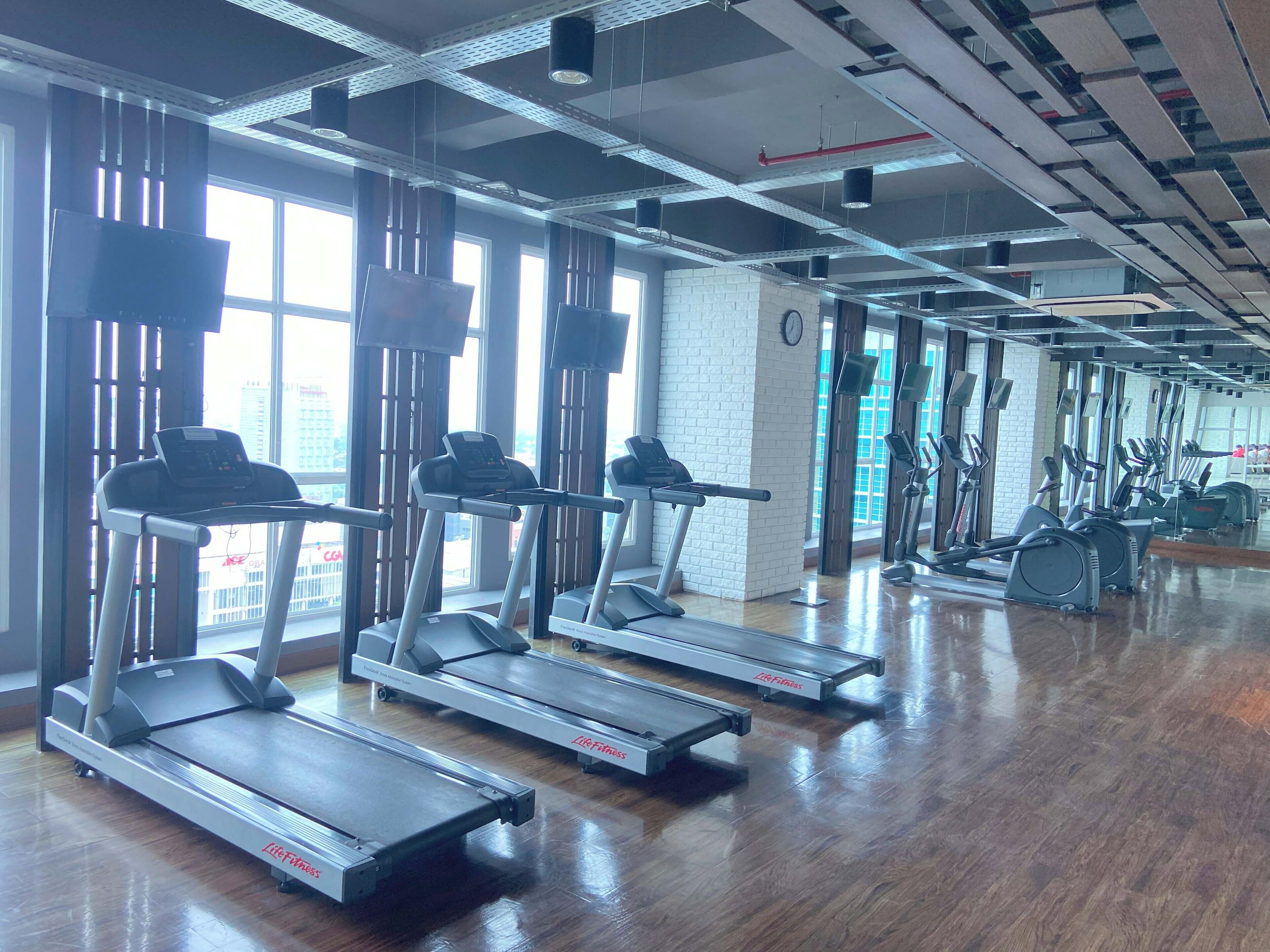 A gym with treadmills, elliptical machines, and a wooden floor.