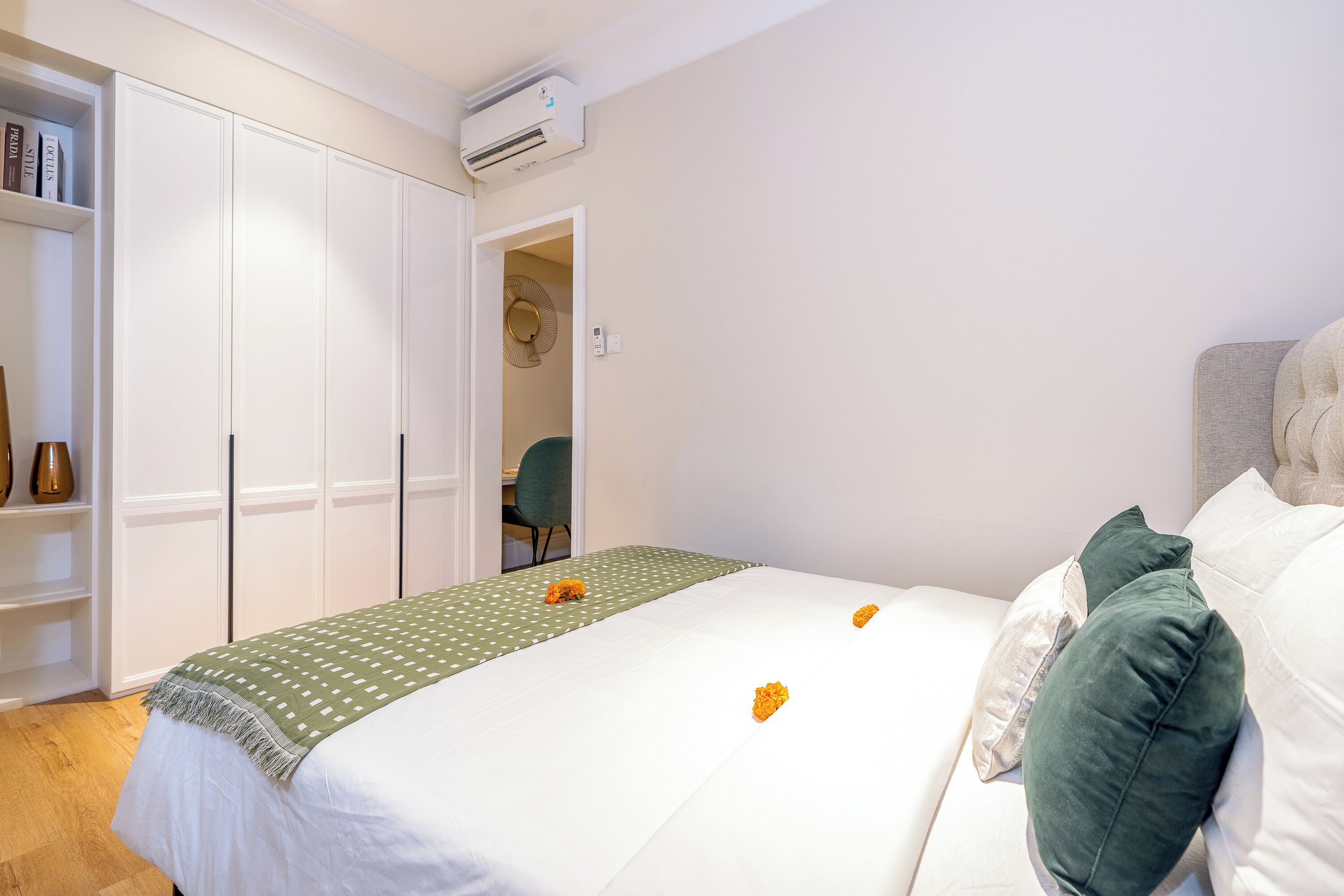 A neatly made bed with a green and white bedspread, a green pillow, and two orange flowers on the bed.