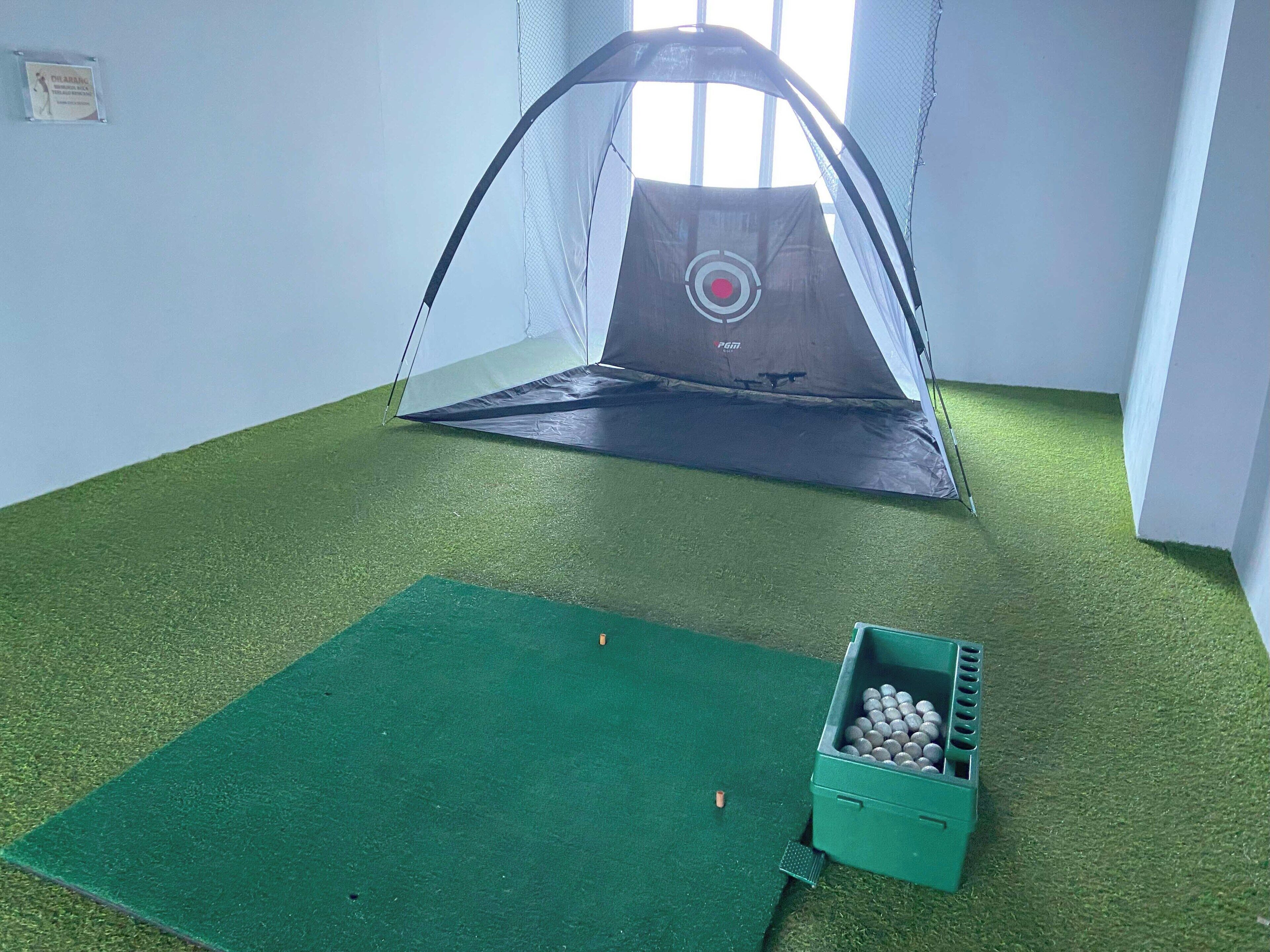 A room with a trampoline and a green mat, a crate with balls, and a window with blinds.