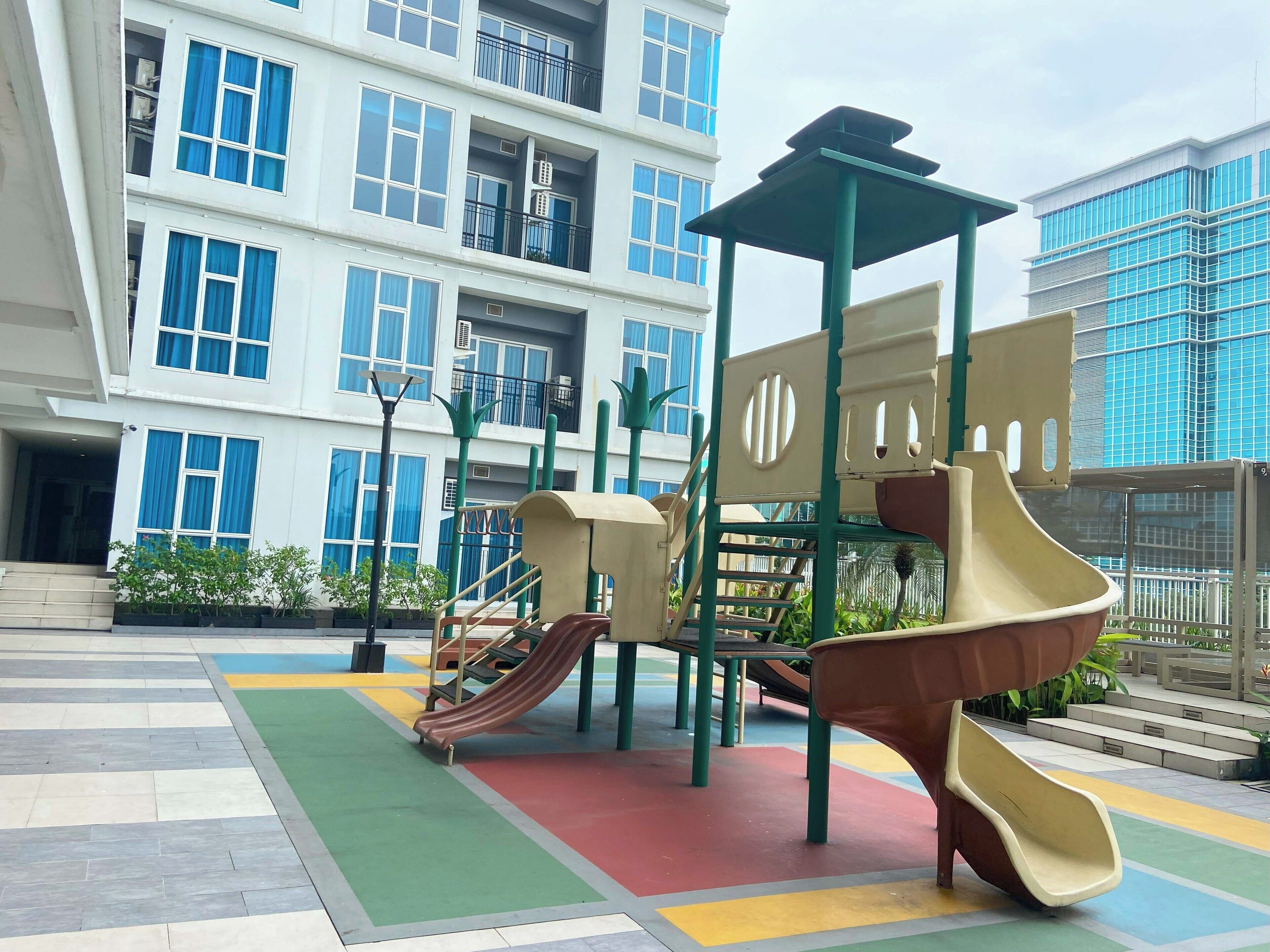 A playground with slides and climbing structures, surrounded by a building with balconies and large windows.