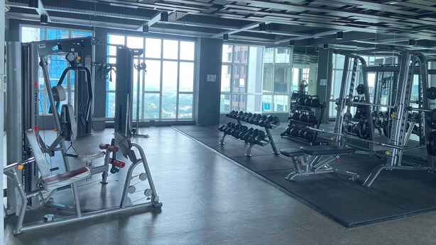 A gym with various exercise equipment, large windows, and a view of the city. - Roseville SOHO and Suites by Nagisa Bali (South Tangerang)