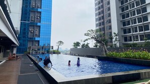 A swimming pool area with a view of high-rise buildings, surrounded by greenery. - Roseville SOHO and Suites by Nagisa Bali (South Tangerang)