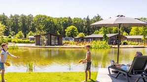 A lakeside setting with a wooden deck, a lounge chair, and a large umbrella.