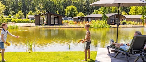 A lakeside setting with a wooden deck, a lounge chair, and a large umbrella.