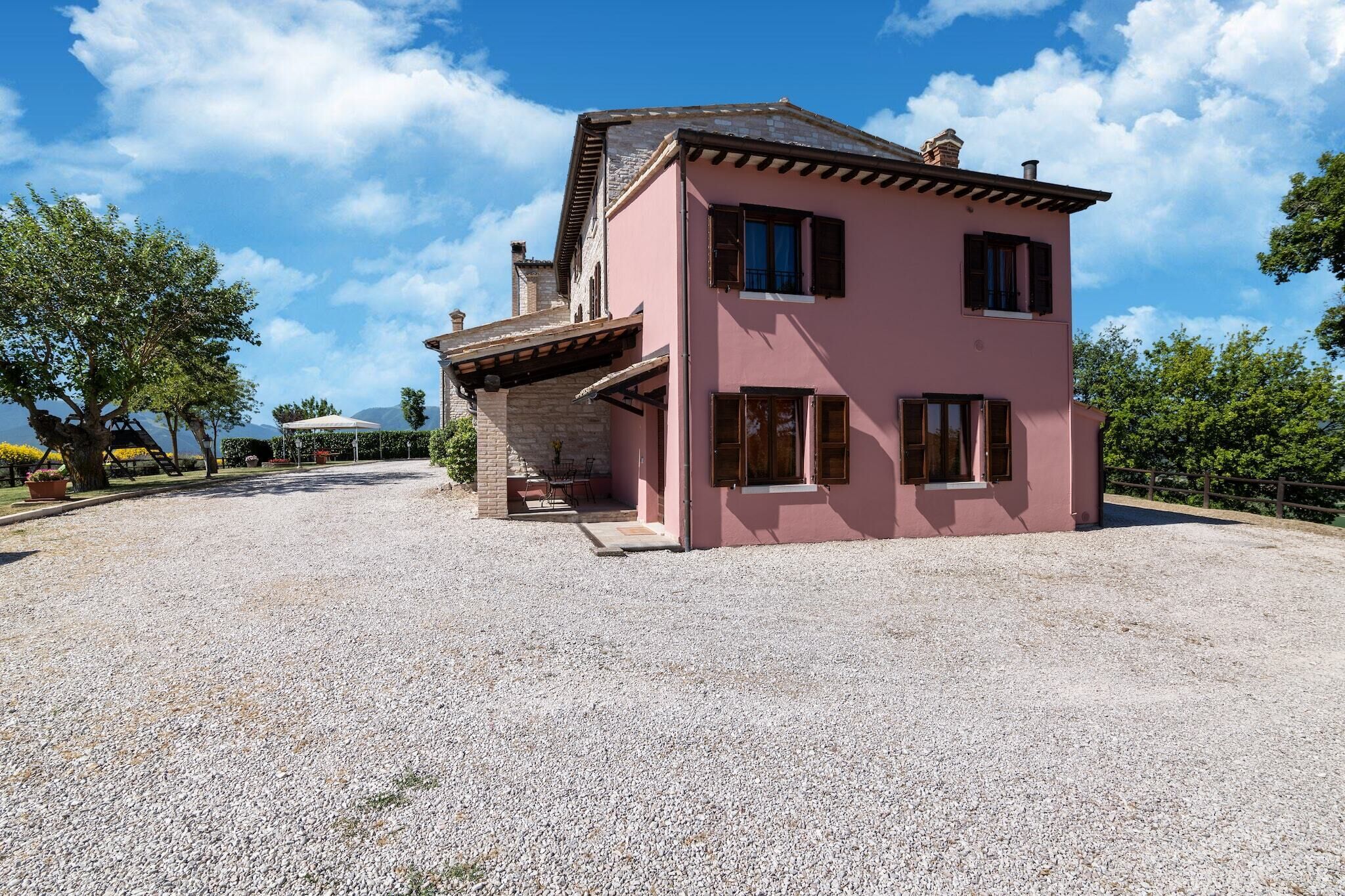 A two-story pink building with a gravel driveway and a covered patio area.