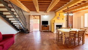 A spacious living area with a wooden staircase, a fireplace, and a dining table with chairs.