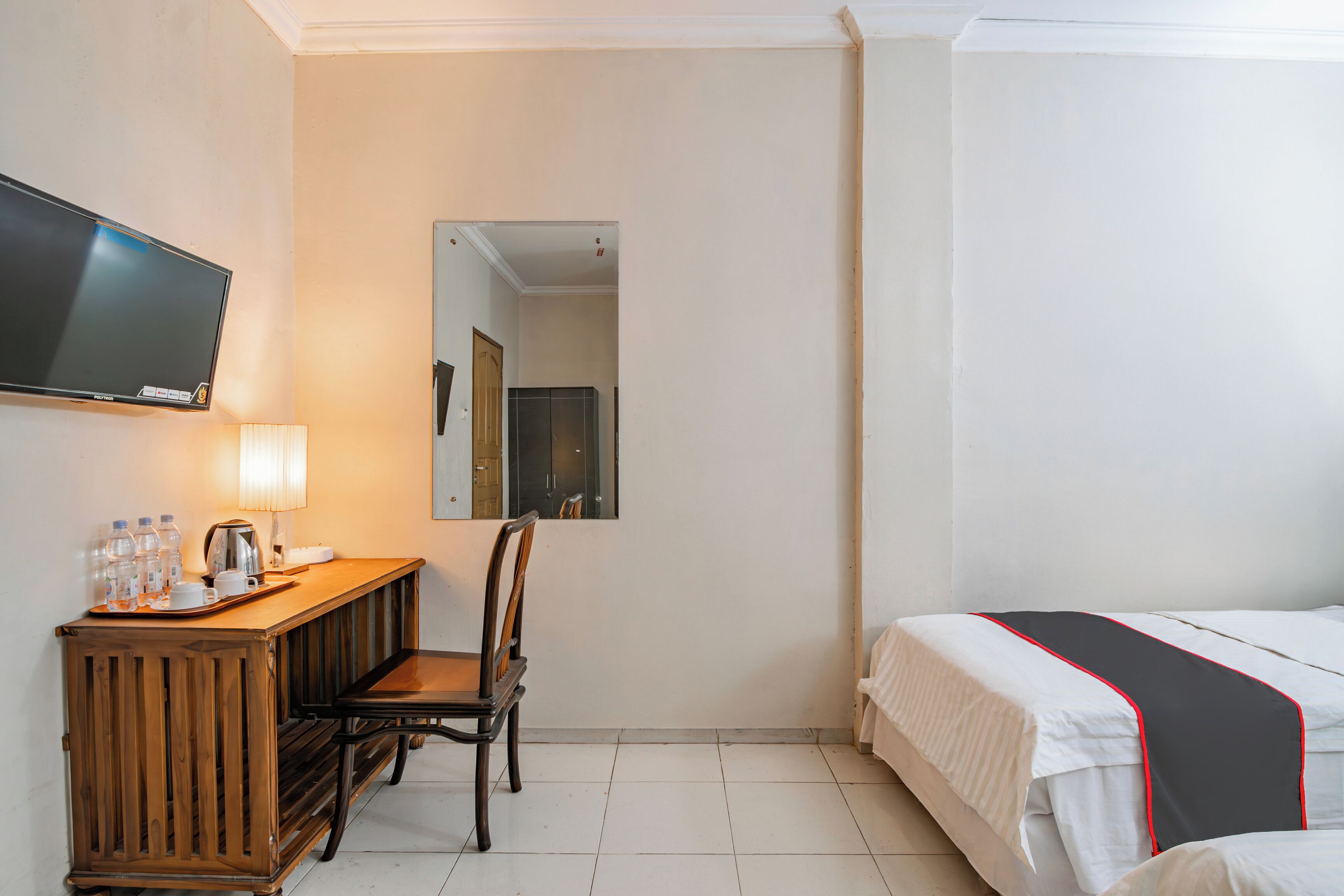A hotel room with a bed, a desk with a chair, a television, and a mirror.