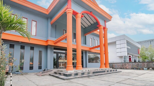 Ein modernes Gebäude mit einer grauen Fassade, orangefarbenen Akzenten und einem überdachten Eingangsbereich mit Säulen.