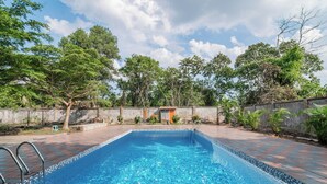 Ein rechteckiger Swimmingpool mit einer gefliesten Kante, umgeben von einer mit roten und grauen Fliesen belegten Fläche.