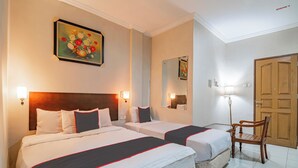 Ein Hotelzimmer mit zwei Betten, einem Holzsessel, einem Bild an der Wand und einer Tür.