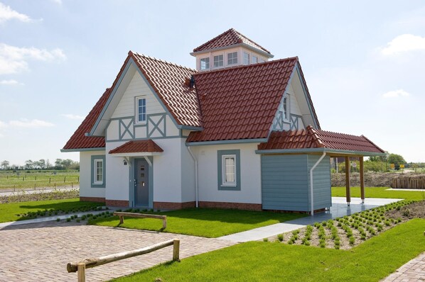 Une maison à deux étages, avec un toit recouvert de tuiles rouges, une petite structure en forme de tour et un porche abrité.