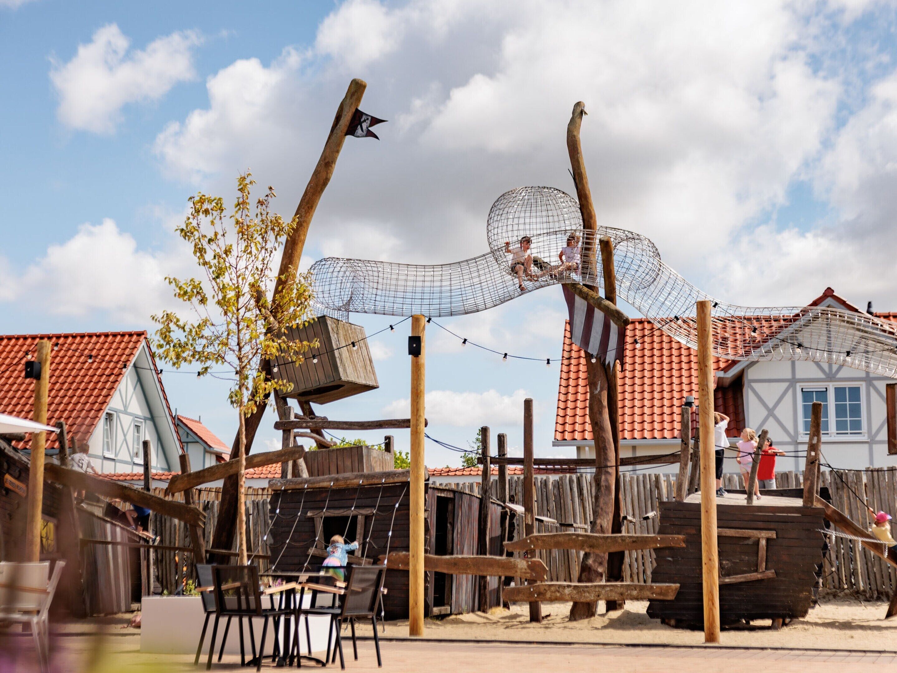 A rustic outdoor play area with wooden structures, including a swing set and a rope bridge.
