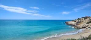 Un paisaje costero con cielo despejado, una playa arenosa y acantilados rocosos.