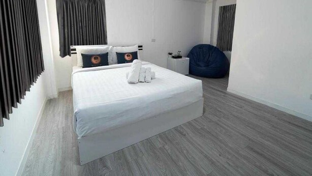 Una habitación de hotel moderna con una cama grande, una mesita de noche, un sillón de peluche y un escritorio pequeño.