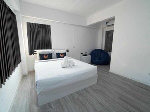 A modern hotel room with a large bed, a bedside table, a bean bag chair, and a small desk. - RQ North Pattaya By Collection O (Pattaya)