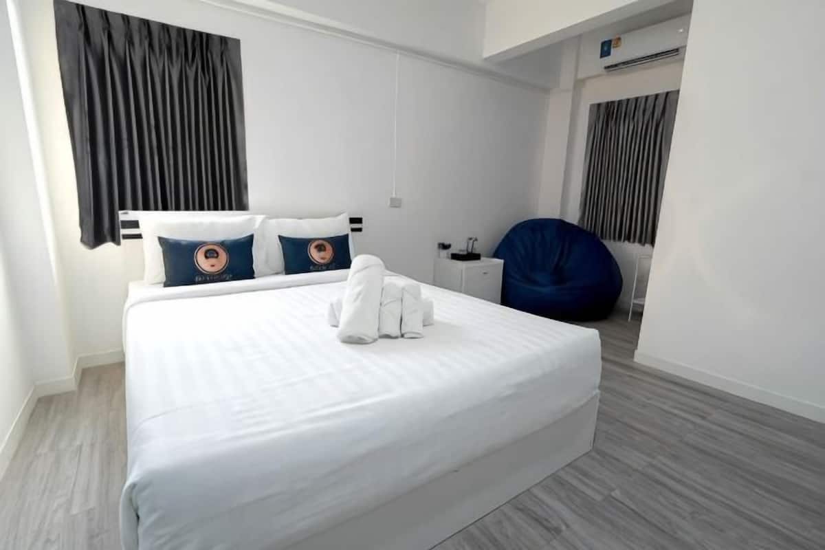 A hotel room with a bed, two pillows, a blue bean bag chair, and a small table.