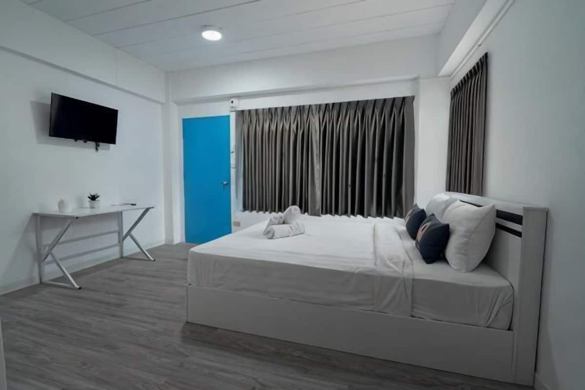 A bedroom with a bed, a desk, a TV, and a blue door.