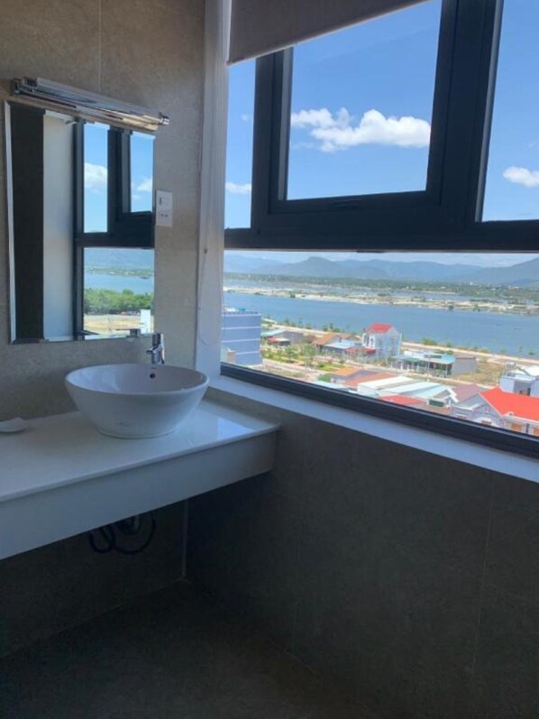 A bathroom with a large window offering a view of a body of water and distant buildings. - Hoàng Sa Bãi Dài (Cam Lam)