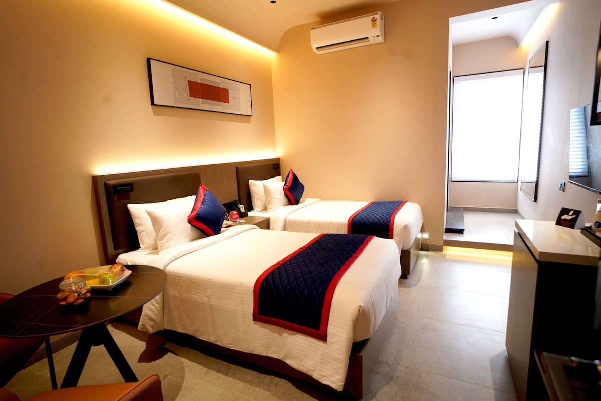 Une chambre d’hôtel avec deux lits, un bureau et une petite table sur laquelle se trouve une assiette de fruits.