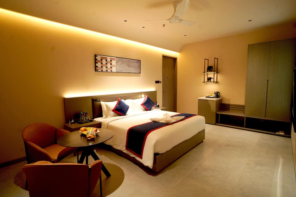 Une chambre d’hôtel comprenant un lit, un coin salon avec une table, une chaise, une petite table avec un saladier de fruits, une table de chevet et une armoire.