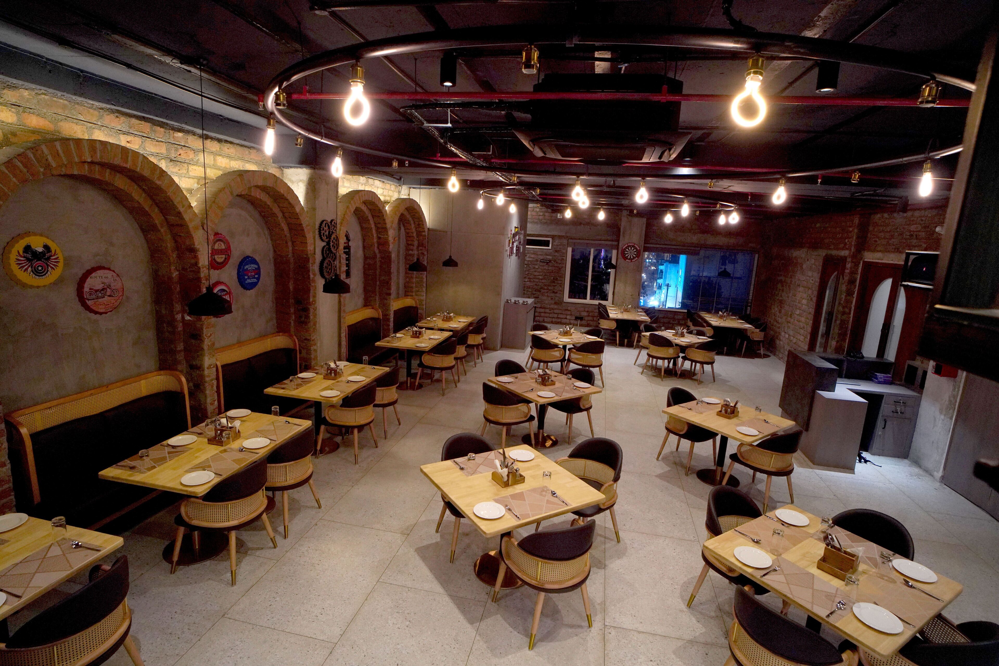 A restaurant with multiple tables and chairs, brick walls, and hanging light bulbs.