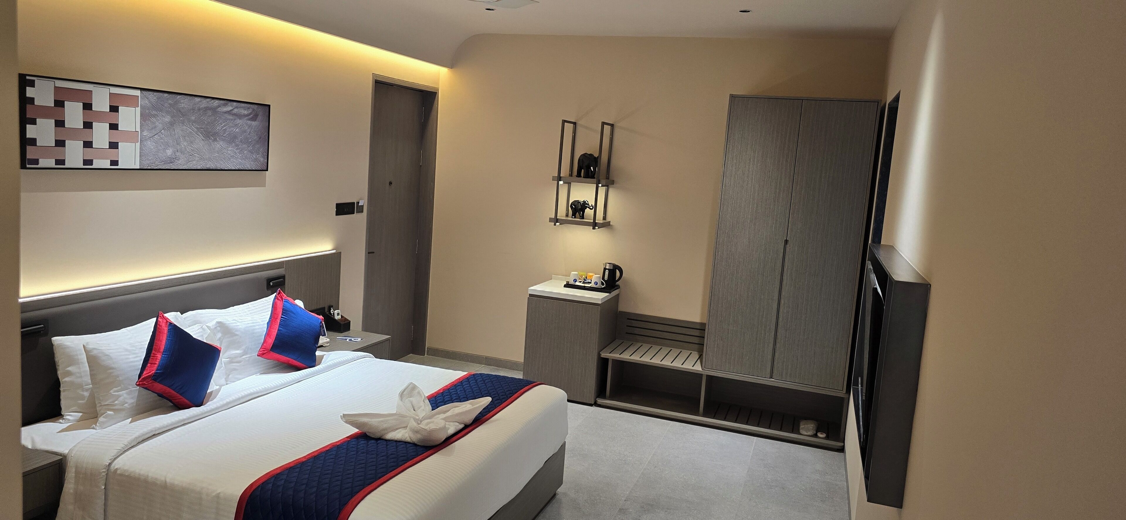 Habitación de hotel con cama, mesita de noche, armario y repisa con cafetera.