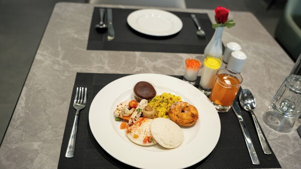 A dining table with a plate of food, a rose in a vase, and various condiments.
