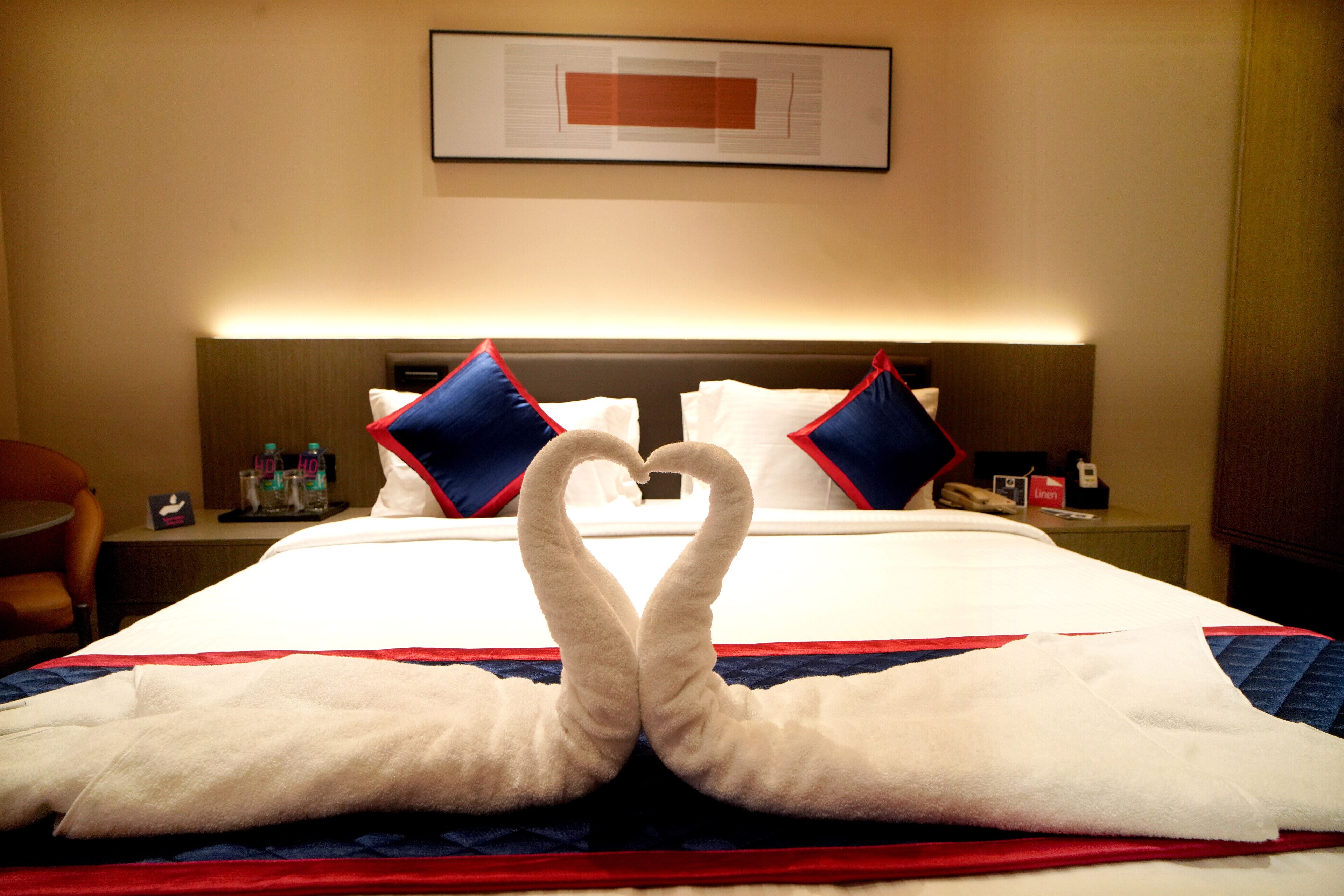 A hotel room with a bed, two pillows, a nightstand, and a framed picture on the wall.