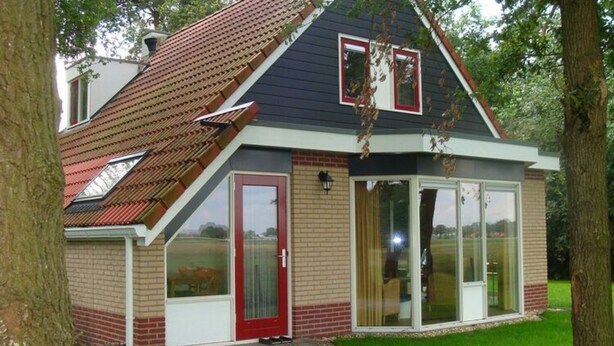 Une petite maison avec une porte rouge, de grandes fenêtres et un toit en pente.