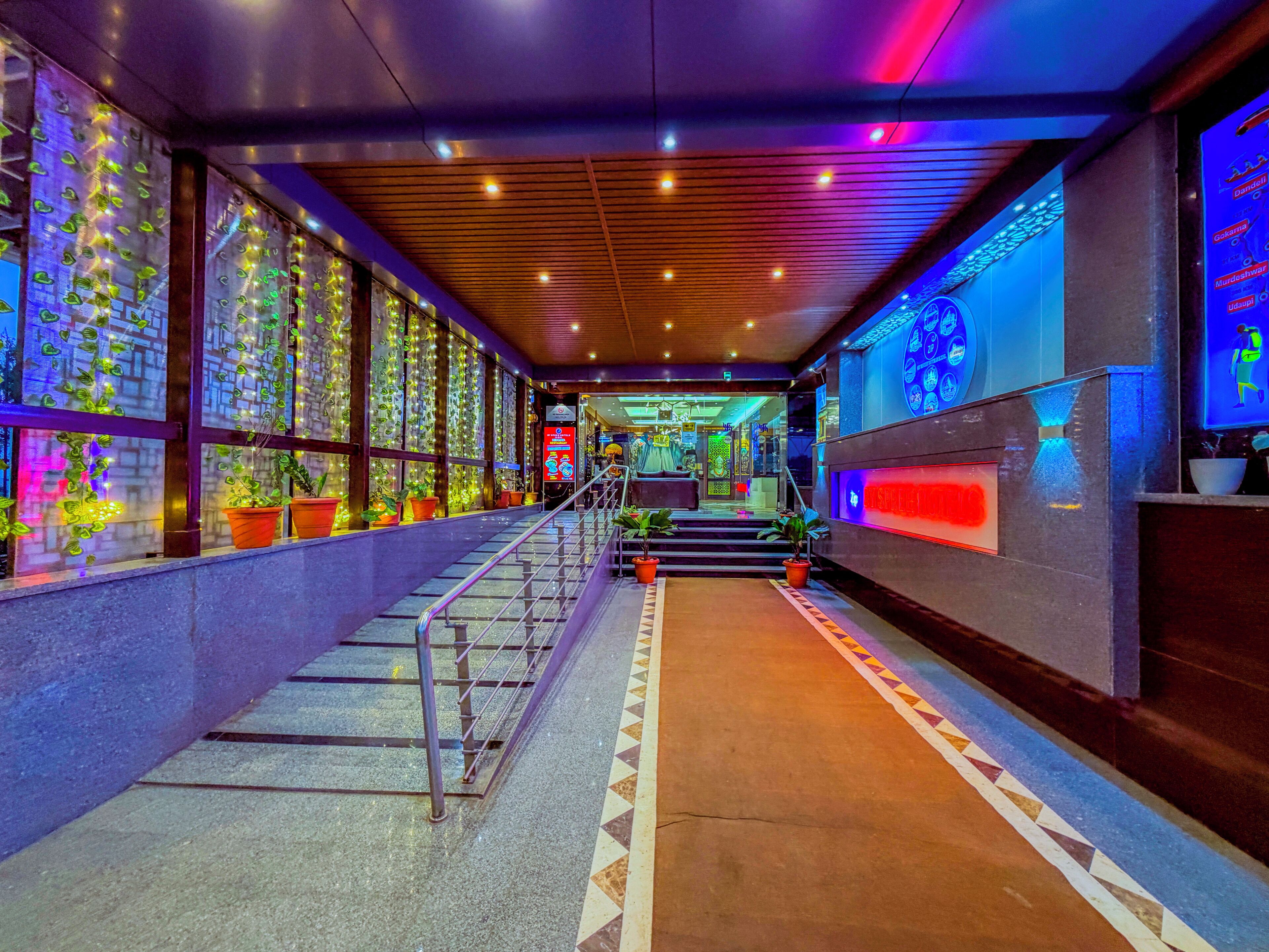 A hallway with a staircase, potted plants, and a digital display.