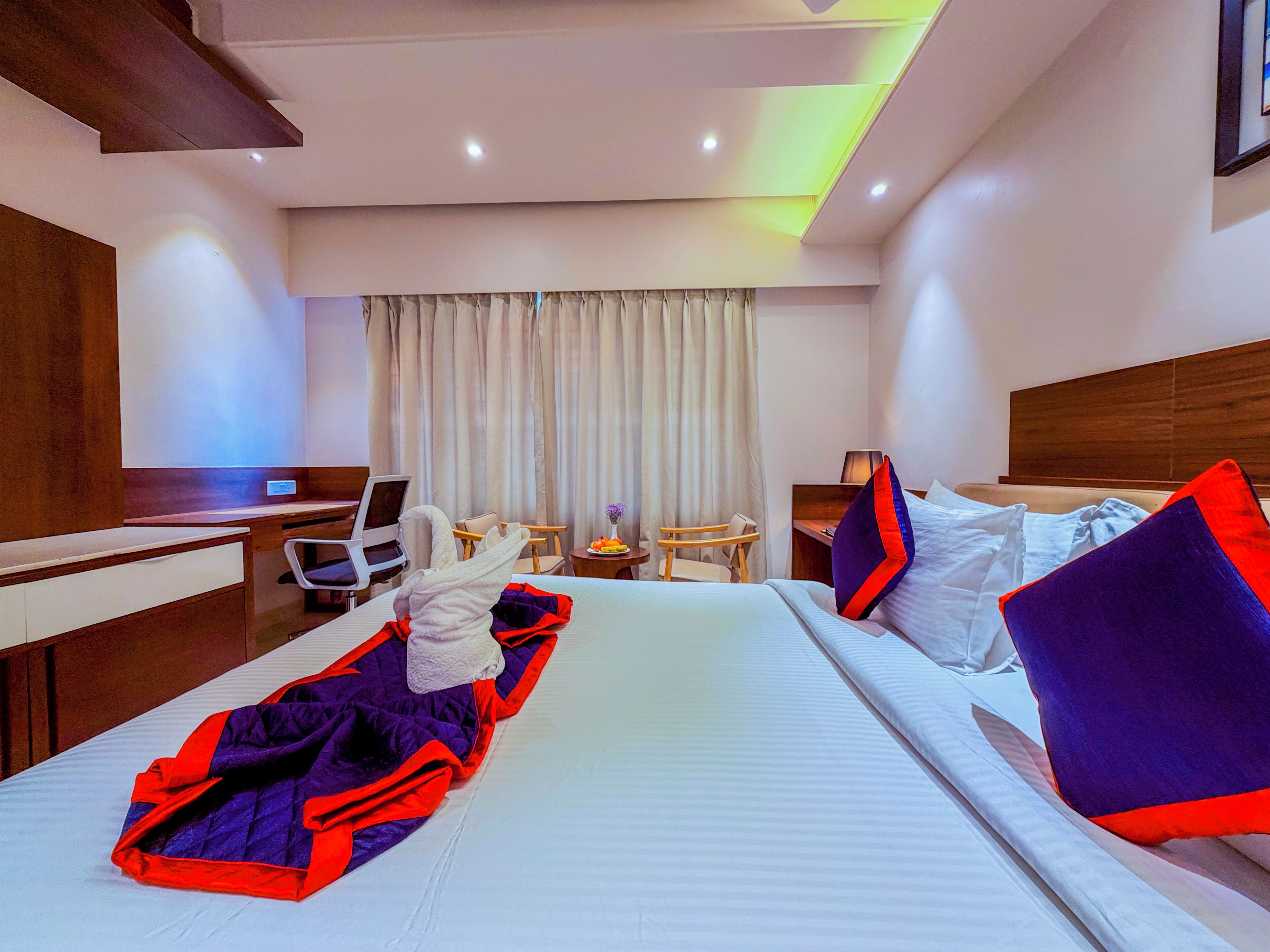 A hotel room with a bed, a desk, a chair, a small table, and a window with curtains.